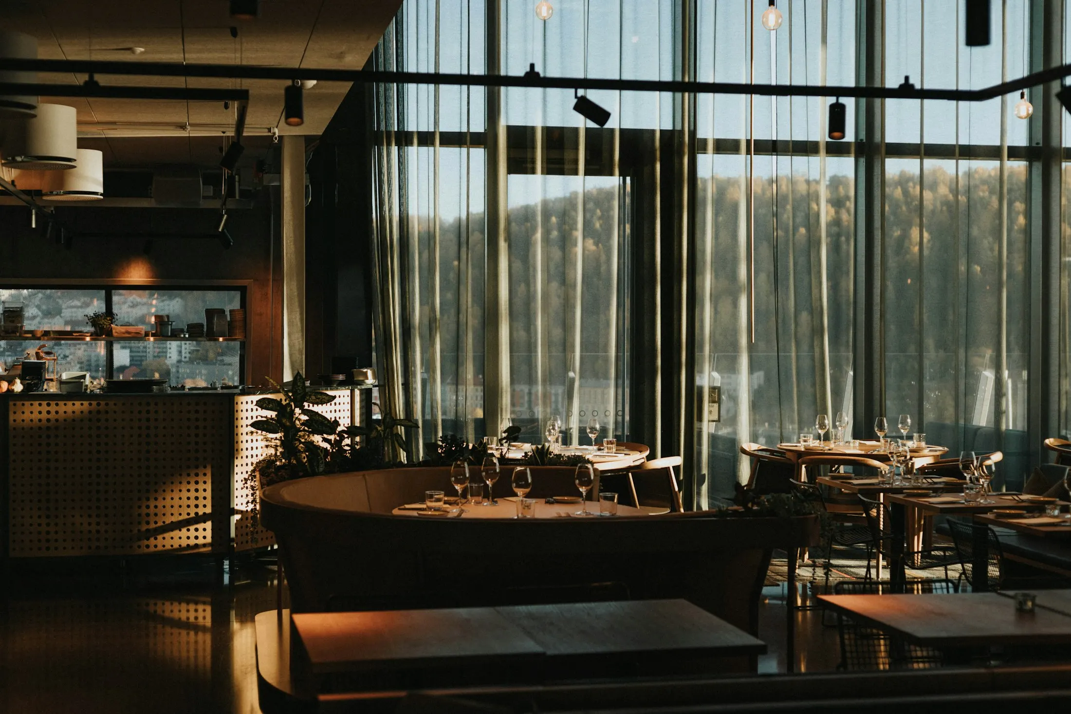 Eingedeckte Tische in einem leeren Restaurant mit großen Fenstern im Abendlicht